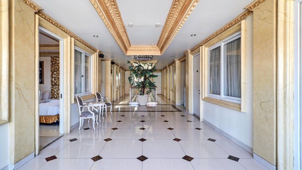 Un pasillo de hotel con piso de baldosas, techo ornamentado y una planta en el centro.
