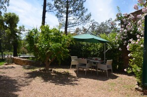 Eine Terrass mit Tisch und Stühlen, umgeben von Bäumen und einer Steinmauer.