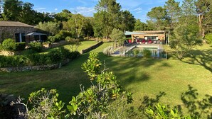 Ein Steinhaus mit Pool, umgeben von einem gepflegten Rasen und Bäumen.