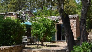 Ein Steinhaus mit einer Terrassenfläche, einem Tisch mit Stühlen und einem Baum mit rosa Blüten.