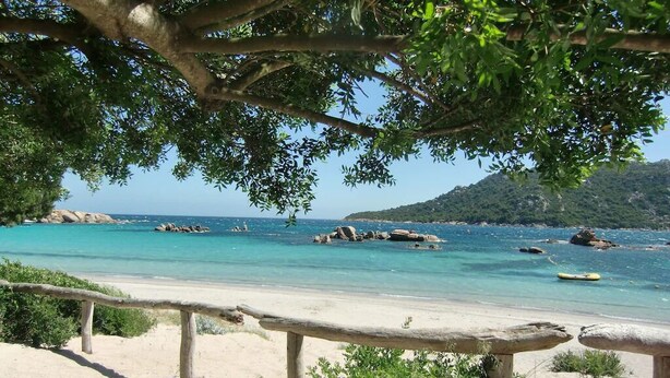 Ein Strand mit einer Holzbrüstung, klarem türkisblauem Wasser und Felsformationen.