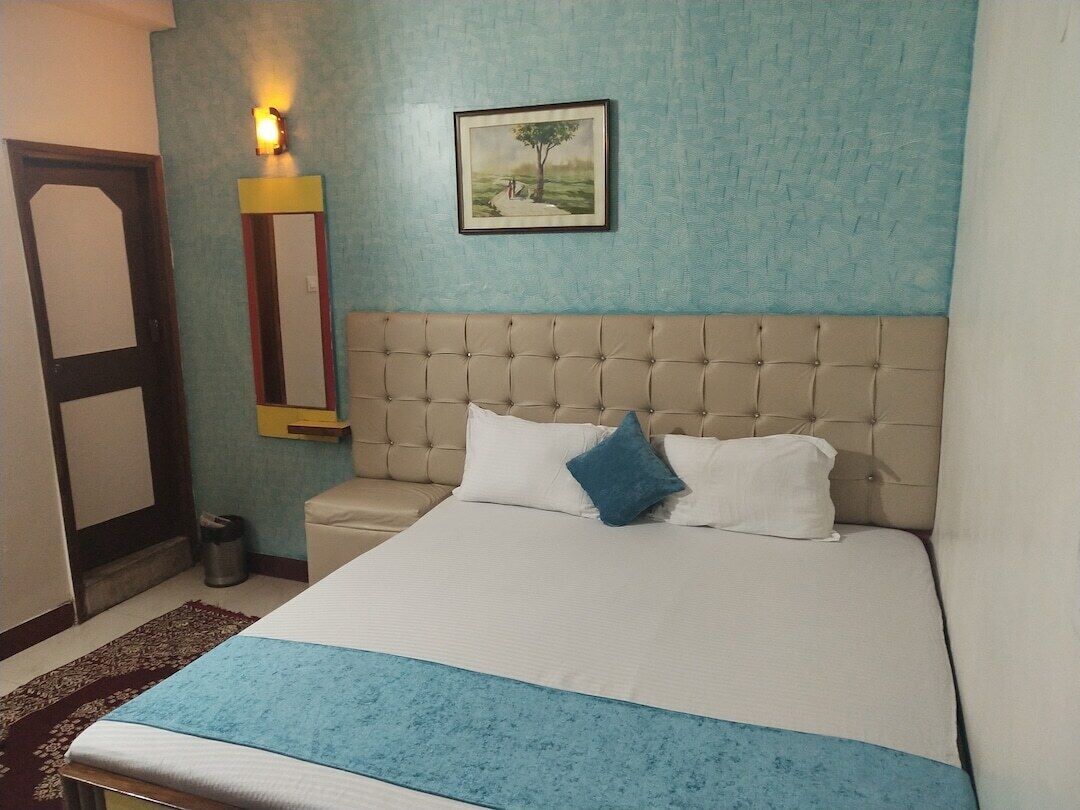 A bedroom with a tufted headboard, a bed with white and blue bedding, a framed landscape painting, a wall-mounted light, and a door with a mirror.