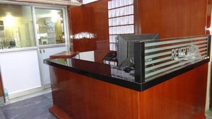 Ein Empfangsschalter mit Holzoptik, einer Glastrennwand und einem Computermonitor.