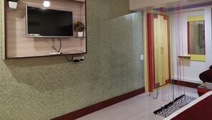 Ein Zimmer mit montiertem Fernseher, einer Pflanze und einem farbenfrohen, gestreiften Raumteiler.