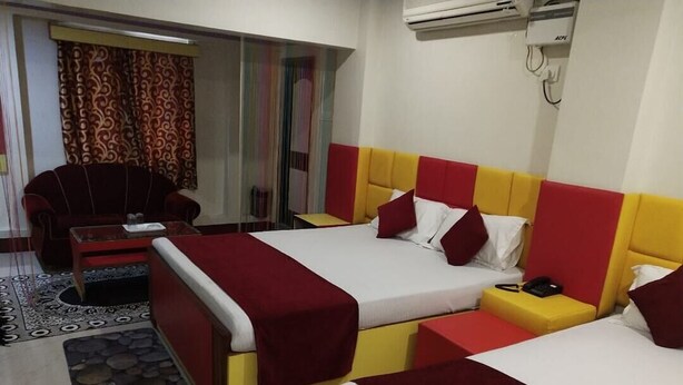 Ein Hotelzimmer mit zwei Betten, einem Sofa, einem kleinen Tisch und einem gemusterten Teppich.