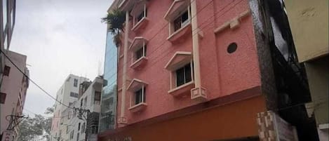 A multi-story building with a red facade, multiple windows, and a gated entrance.