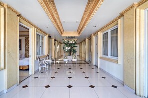Ein Hotelkorridor mit Fliesenboden, aufwändigem Deckenstuck und einer Topfpflanze in der Mitte.
