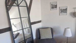 A room with a large mirror, a bed, a chair, a lamp, and framed pictures on the wall. - APARTMENT PANORAMIC VIEW OF PETITE VENISE PARKING (Colmar)