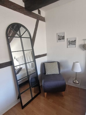 A room with a large mirror, a bed, a chair, a lamp, and framed pictures on the wall. - APARTMENT PANORAMIC VIEW OF PETITE VENISE PARKING (Colmar)