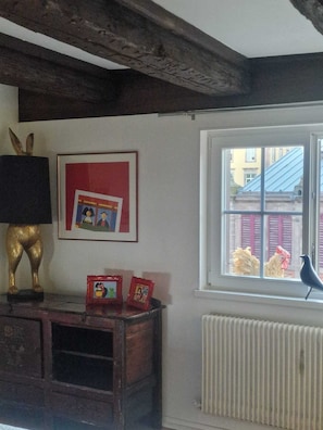 A room with a radiator, a window with a view of buildings, a framed picture on the wall, and a bird on the windowsill. - APARTMENT PANORAMIC VIEW OF PETITE VENISE PARKING (Colmar)