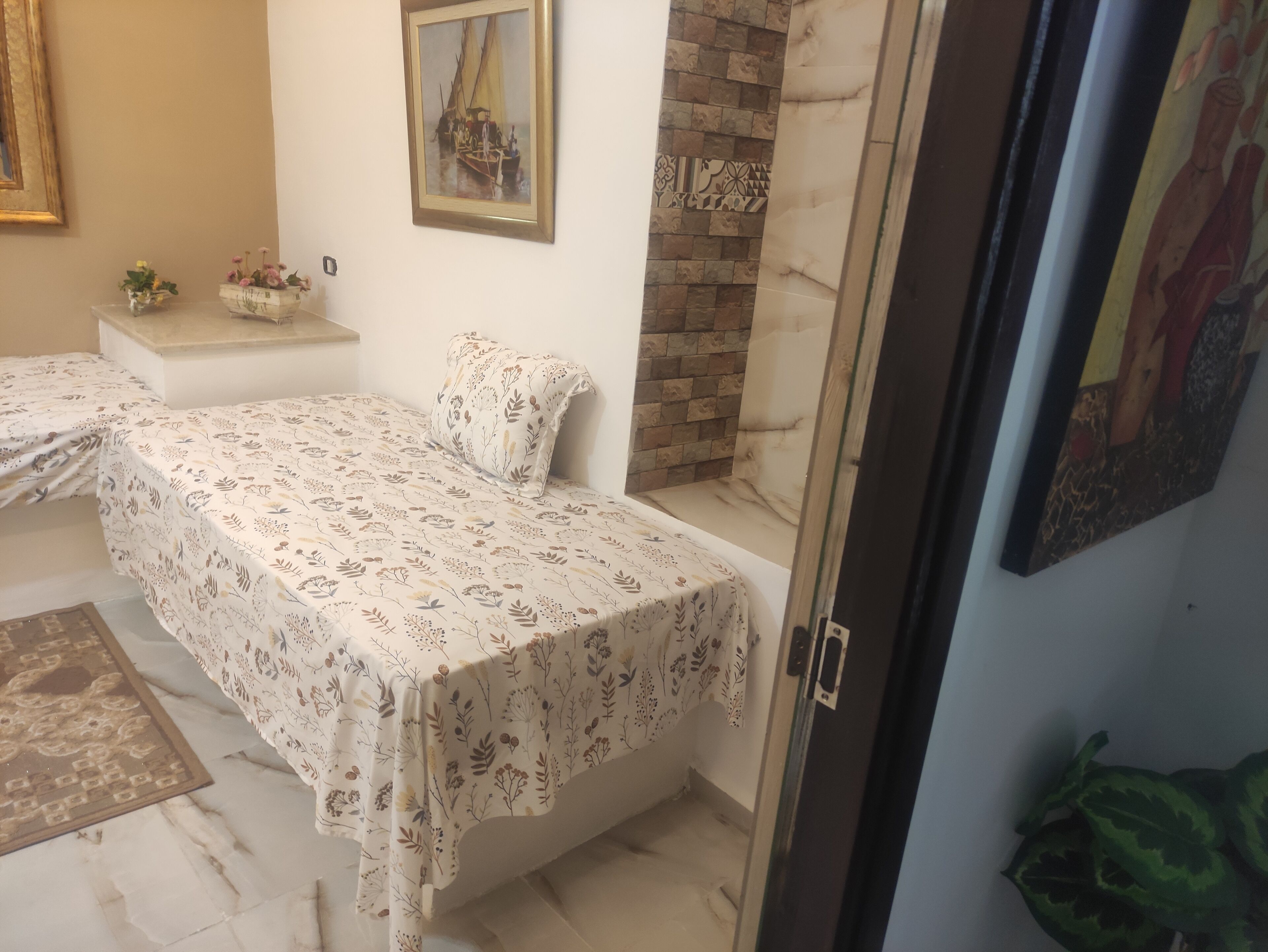 Une chambre à coucher comprenant un lit, une petite table de chevet, un tableau accroché au mur et une porte donnant sur une autre pièce.