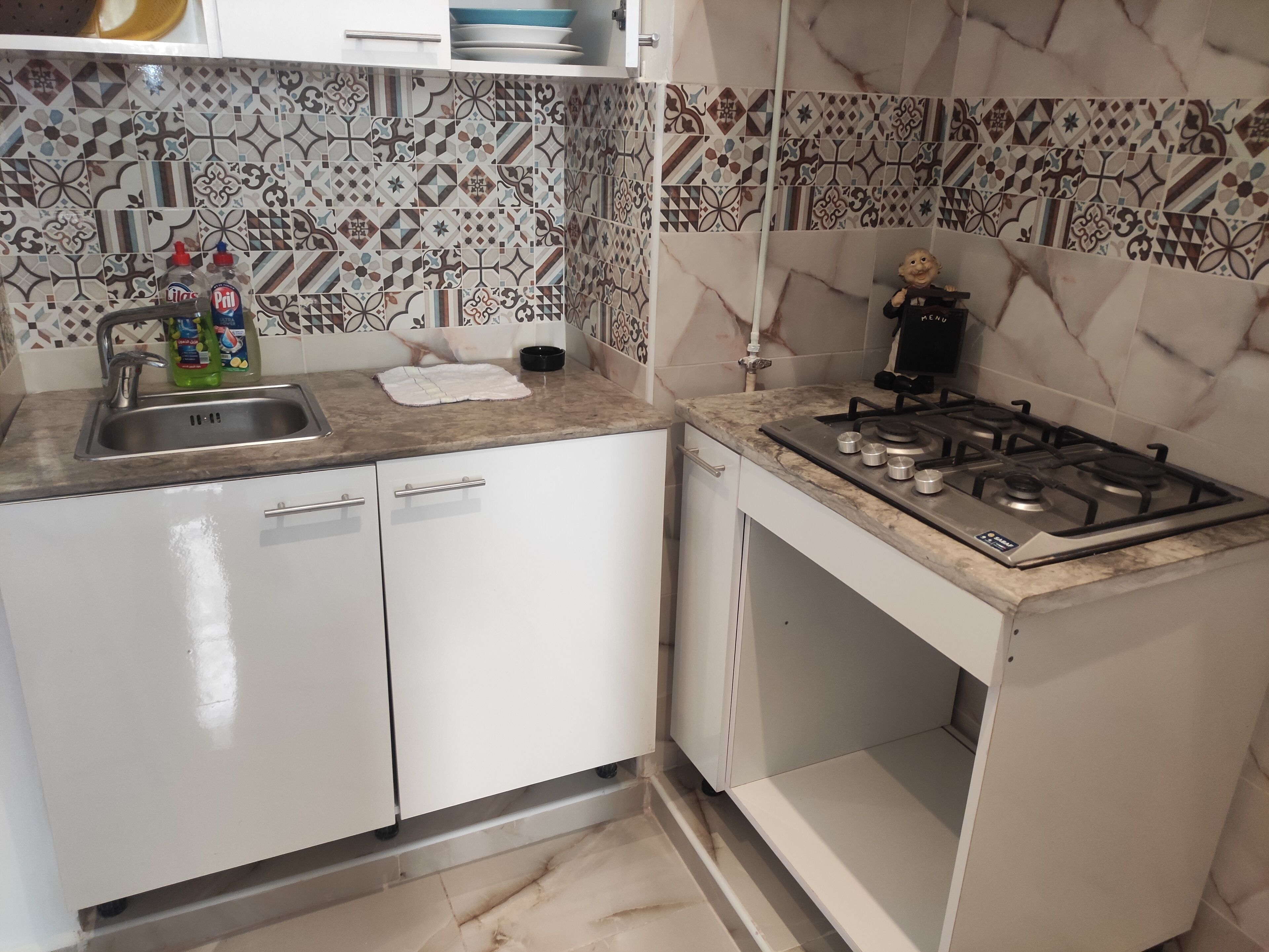 Una cocina con estufa a gas, pileta y muebles blancos.