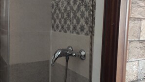 Zona de ducha con cabezal, ducha de mano y mandos en la pared.