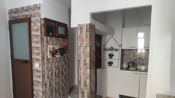 Un pasillo con una puerta, una pared con diseño de ladrillo y una zona de cocina con armarios blancos y salpicadero de azulejos.