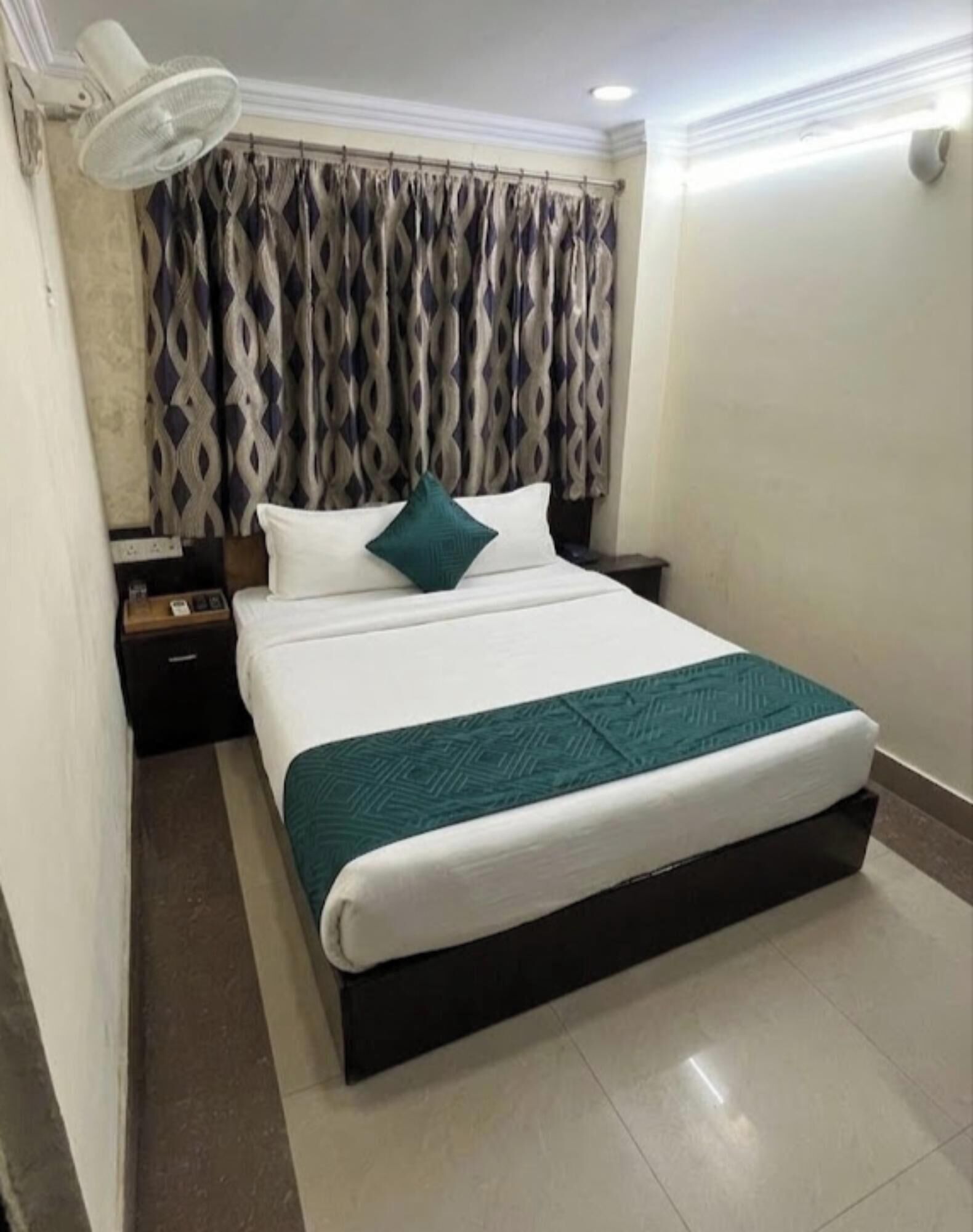 A hotel room with a large bed, a nightstand, a lamp, and patterned curtains.