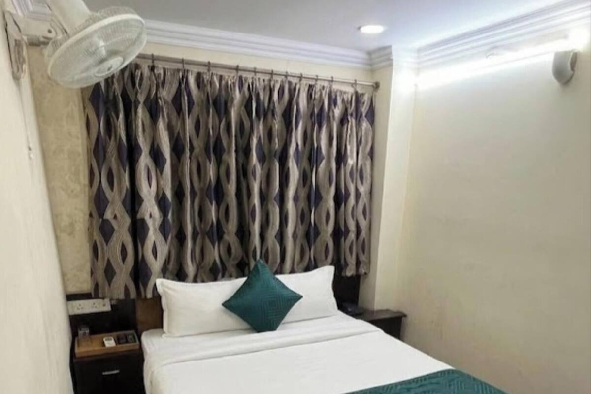 A hotel room with a large bed, a nightstand, a lamp, and patterned curtains.