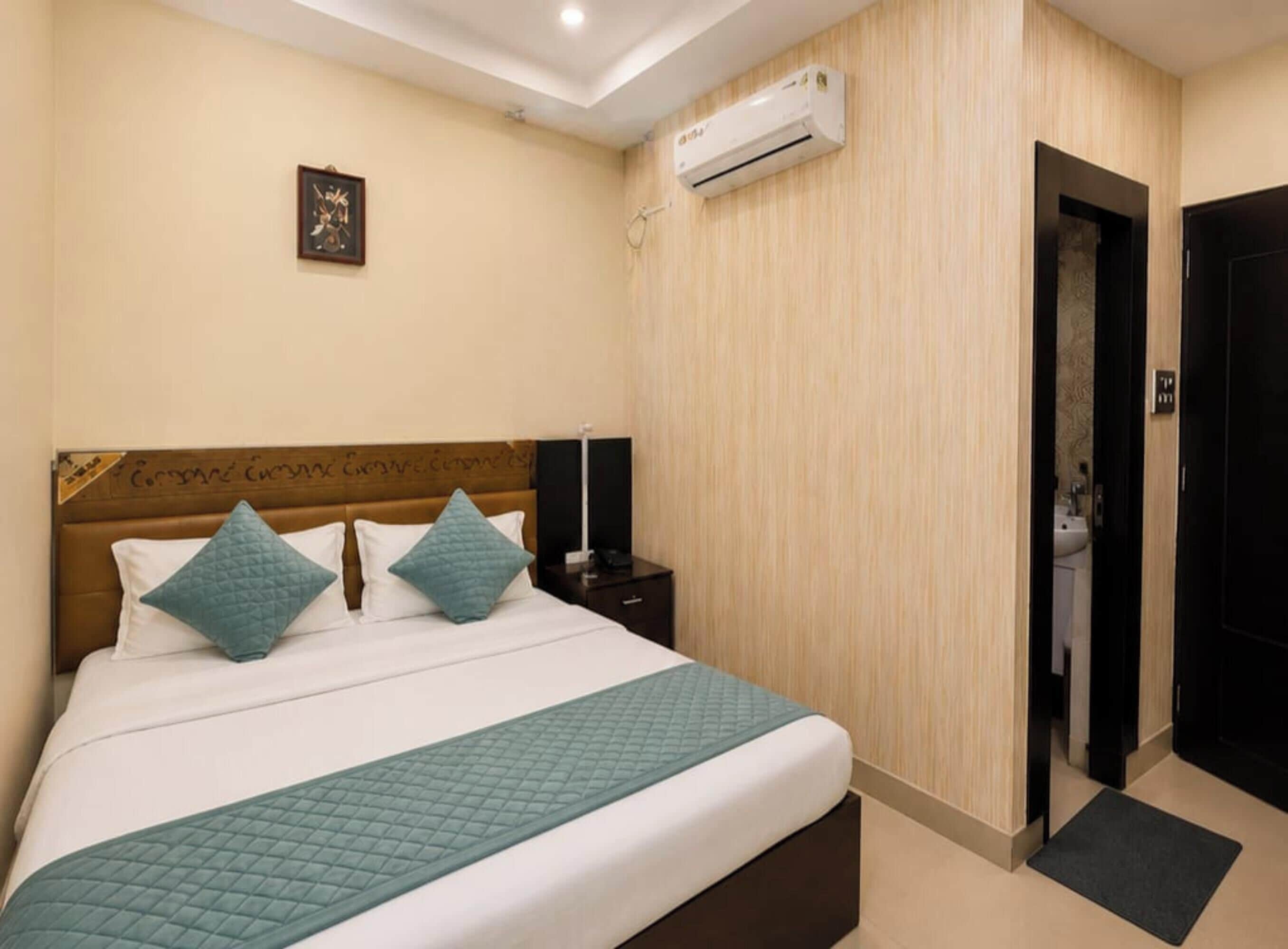 A hotel room with a bed, an air conditioning unit, a door, and a wall-mounted picture.