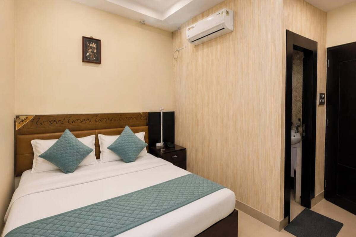 A hotel room with a bed, an air conditioning unit, a door, and a wall-mounted picture.