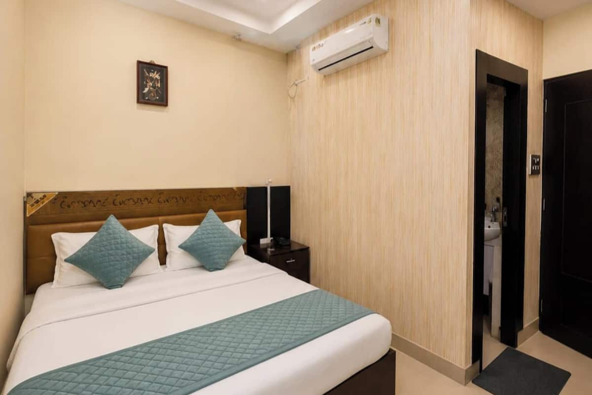 Habitación de hotel con cama, unidad de aire acondicionado, puerta e imagen colgada en la pared.