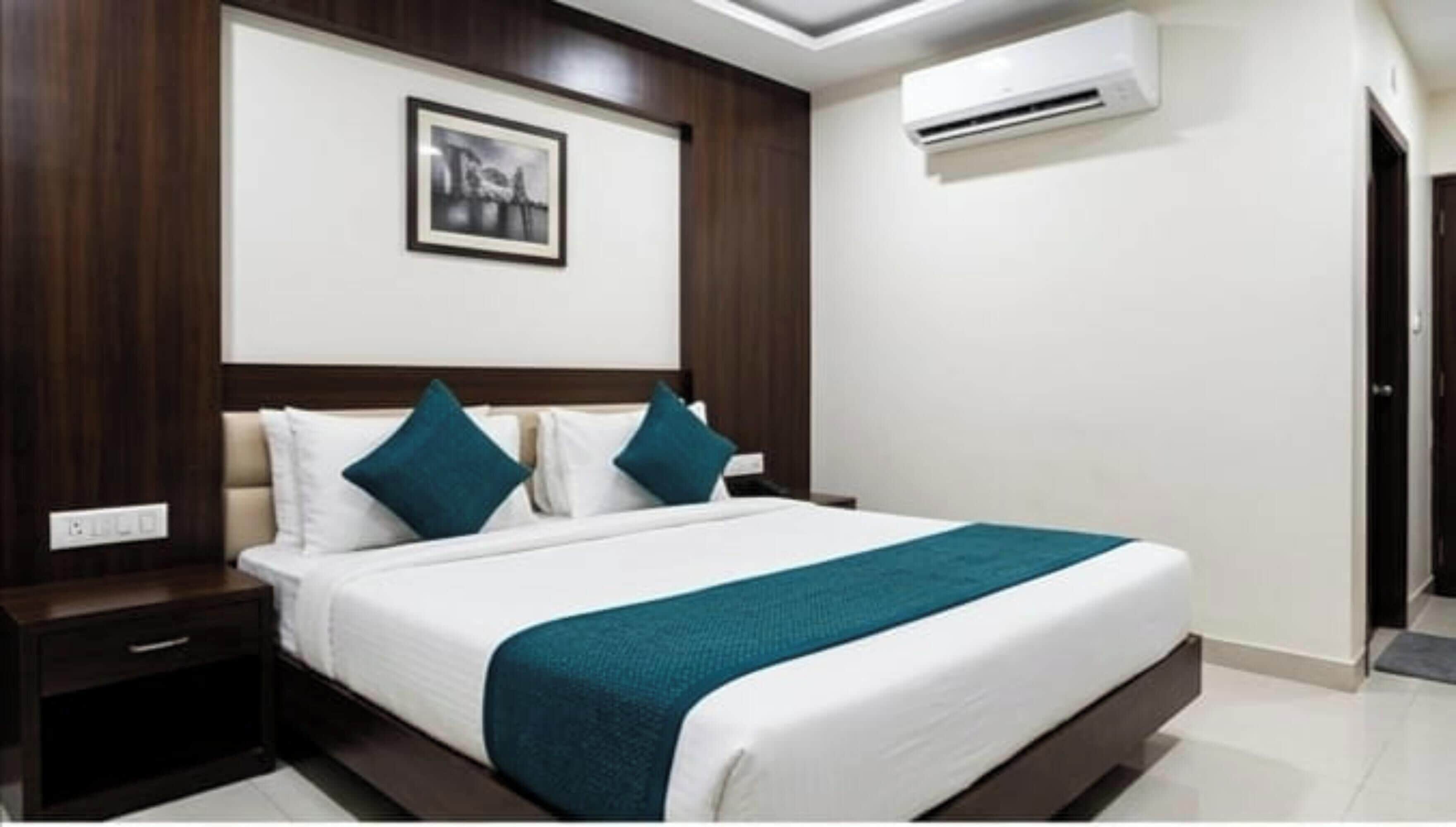 A hotel room with a bed, a nightstand, a wall-mounted air conditioner, and a framed picture above the bed.