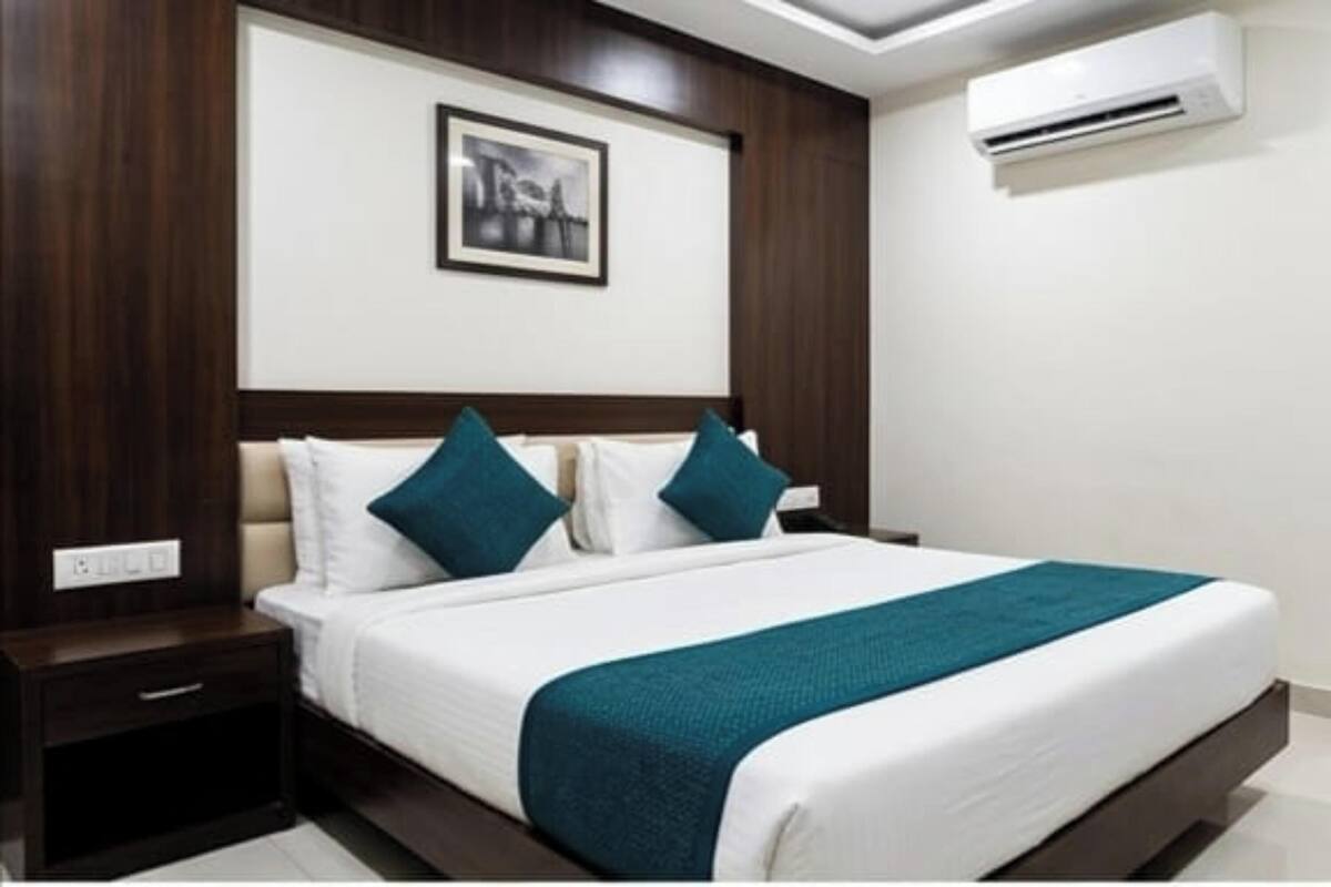 A hotel room with a bed, a nightstand, a wall-mounted air conditioner, and a framed picture above the bed.