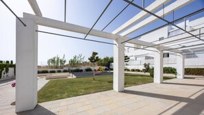 Un espace extérieur doté d’une structure en verre, d’un chemin pavé et d’une zone herbeuse avec un espace de jeux pour enfants.