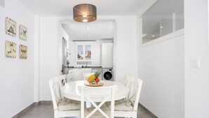 Une cuisine moderne avec des meubles blancs, une table à manger avec des chaises et un panier de fruits posé sur la table.