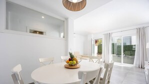 Un espace repas moderne avec une table ronde, des chaises blanches et un saladier rempli de fruits.