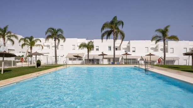 Une piscine bordée de palmiers, avec des bâtiments blancs en arrière-plan.