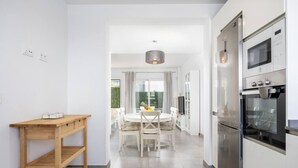 Une cuisine moderne avec des armoires blanches, un four encastré et un coin repas comprenant une table ronde et des chaises.