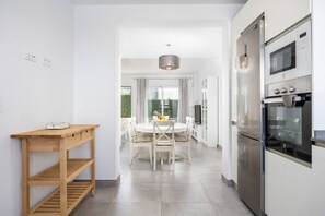 Eine moderne Küche mit weißen Schränken, einem Einbauofen und einem Essbereich mit rundem Tisch und Stühlen.