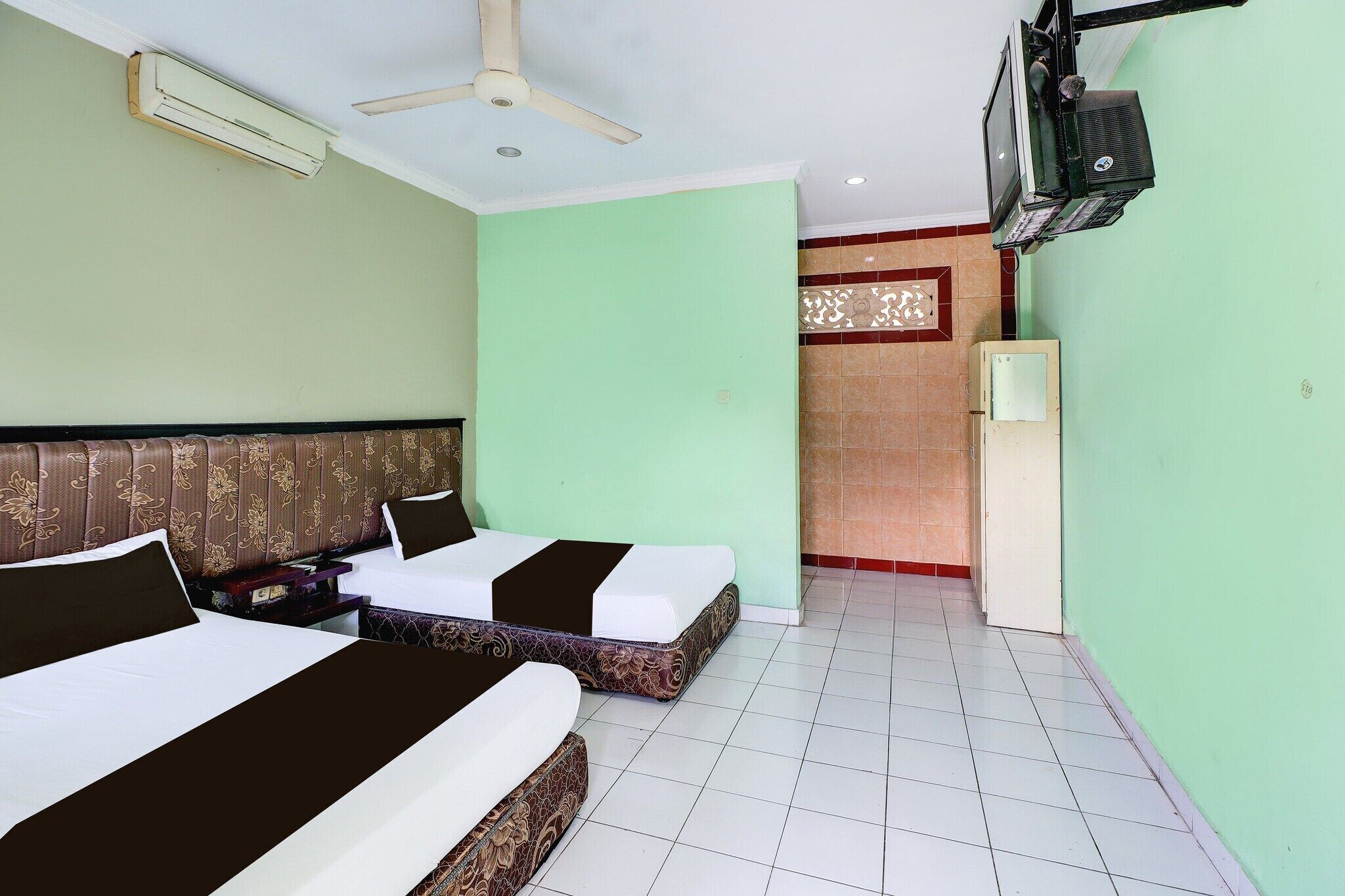 Quarto de hotel com duas camas, ventoinha no teto, ar condicionado, televisão e chão revestido de azulejos.