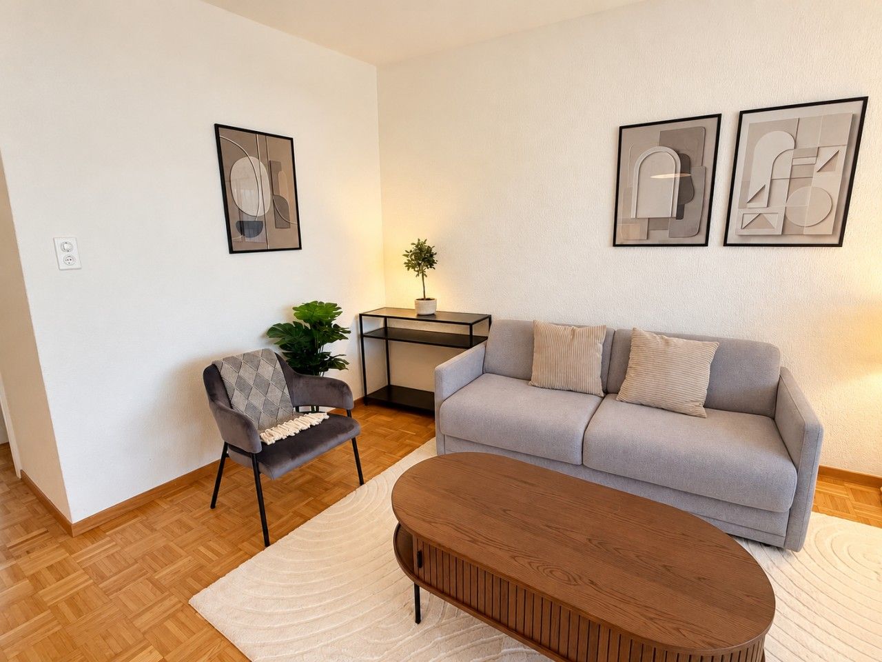 Un salon avec un canapé gris, une table basse en bois, un fauteuil gris et une petite table d’appoint sur laquelle est posée une plante.