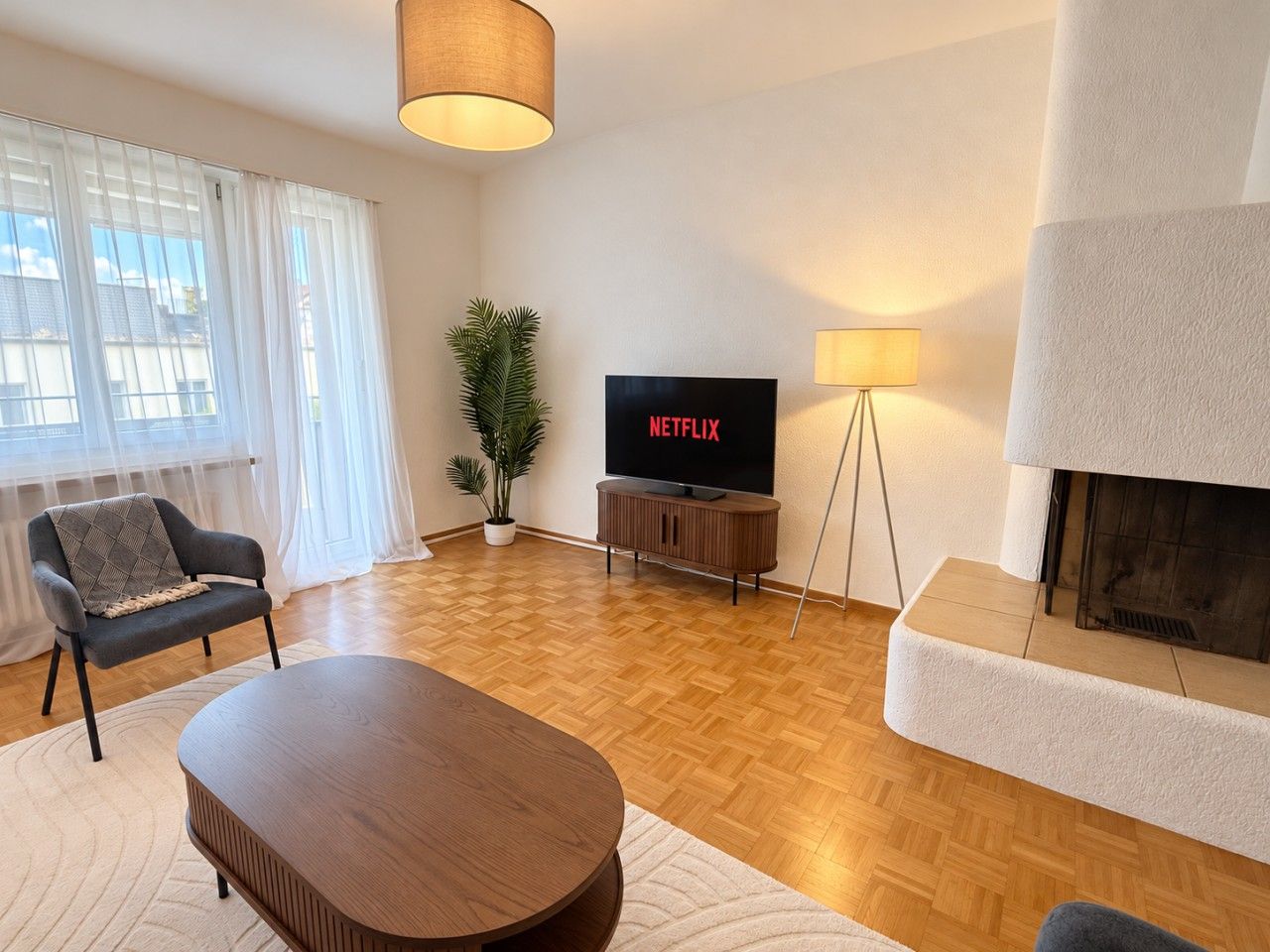 A living room with a television, a sofa, a coffee table, a fireplace, and a plant.