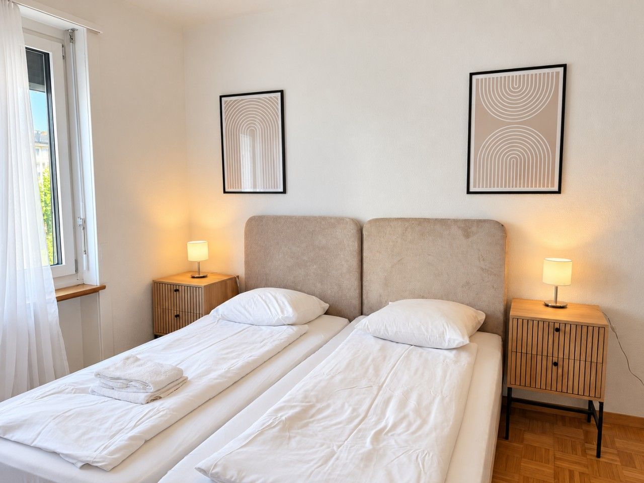 Ein Doppelbett mit weißen Leinentüchern, zwei Nachttische mit Lampen sowie zwei gerahmte Wandbilder.