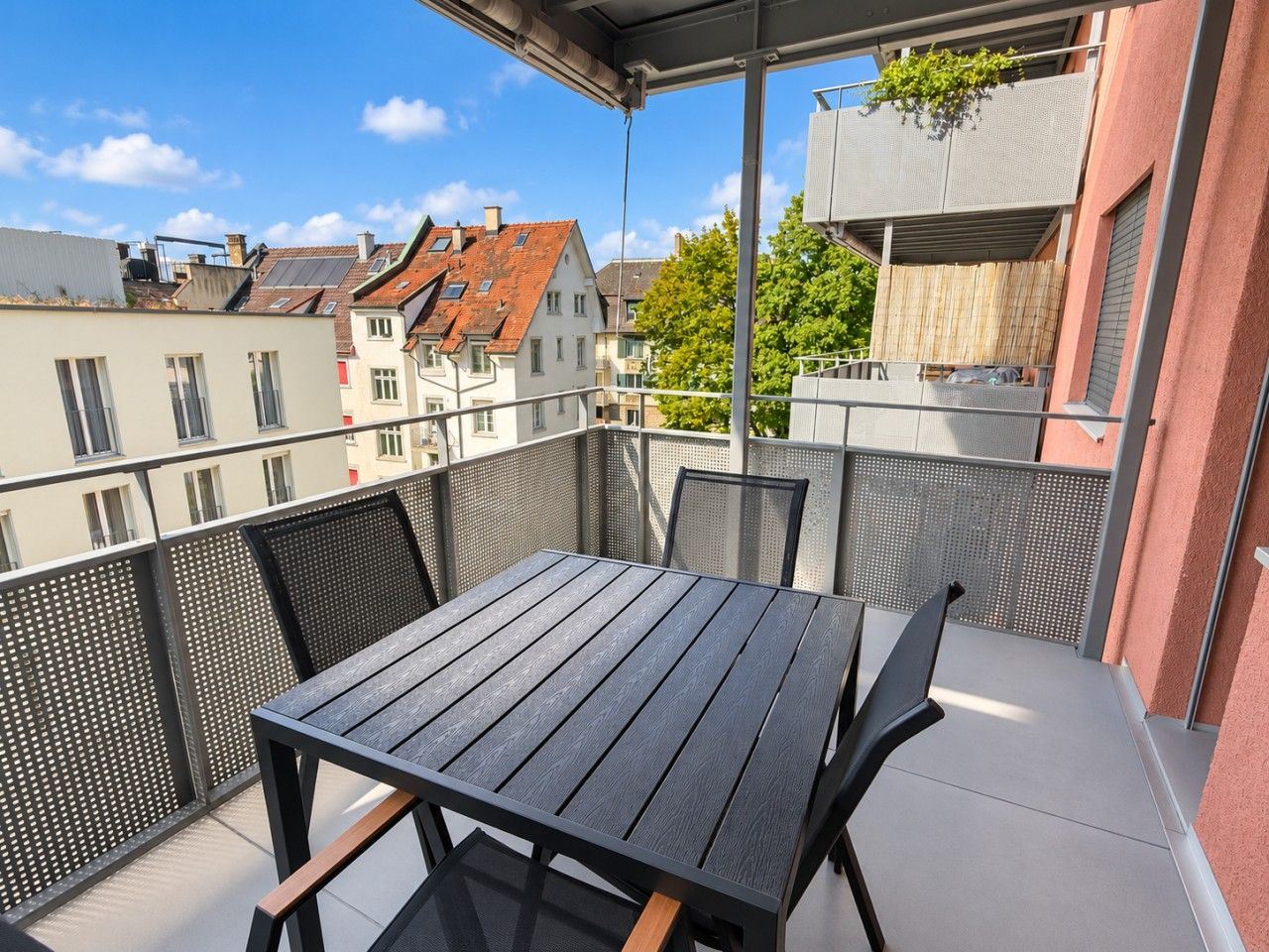 A balcony with a table and chairs, overlooking a residential area with houses and trees.