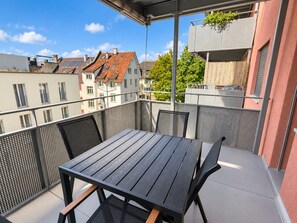A balcony with a table and chairs, overlooking a residential area with houses and trees. - Central 2BR with Superbe Transit Access - Tilia 21 (Zürich)