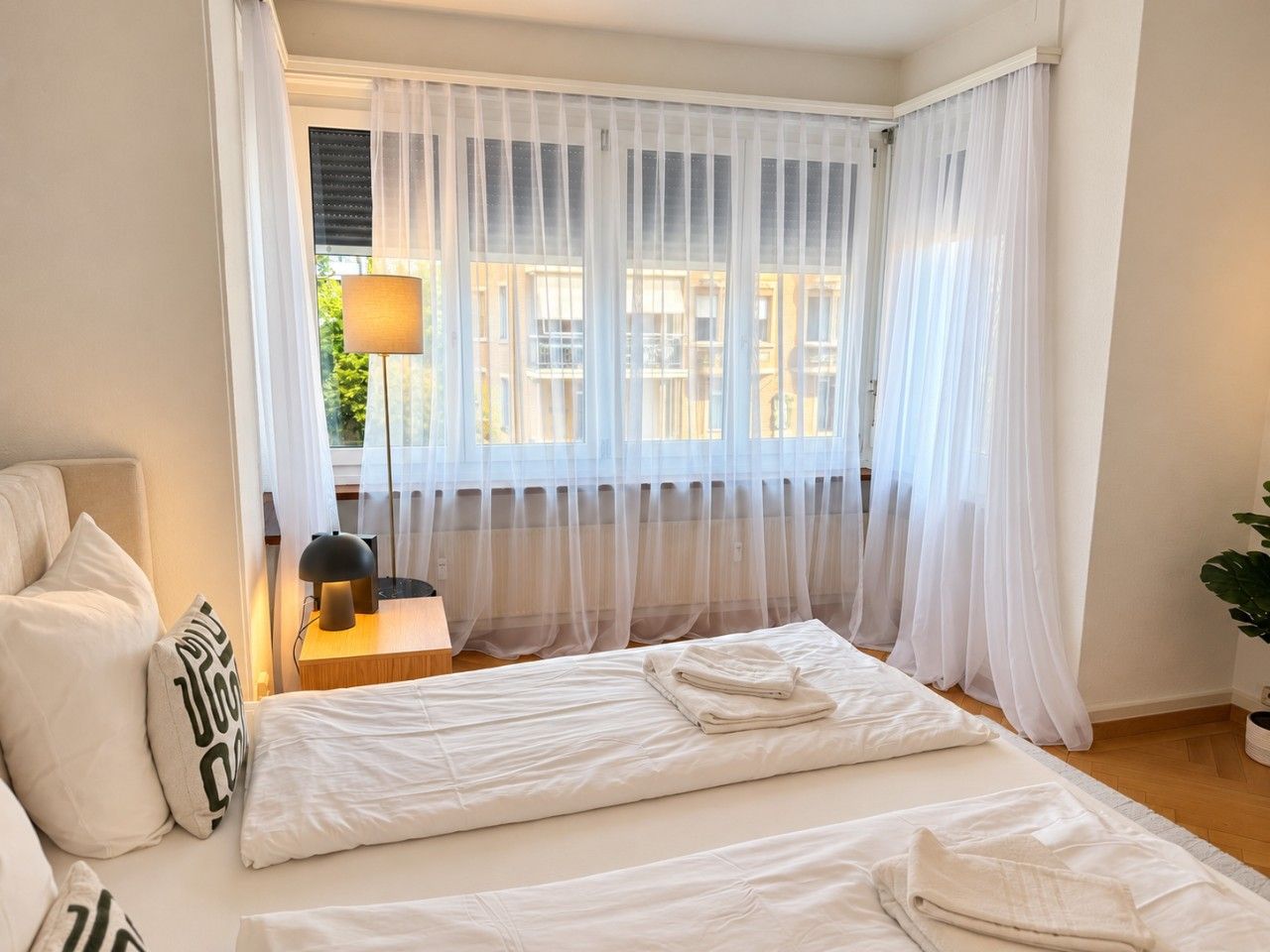 Une chambre d’hôtel avec un lit, une table de chevet avec une lampe et des rideaux légers.
