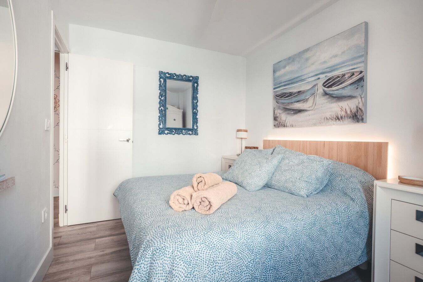 Une chambre à coucher avec un lit, un miroir, un tableau et une table de chevet.