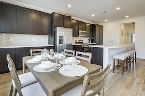 A modern kitchen with dark cabinets, stainless steel appliances, and a wooden dining table set for four.
