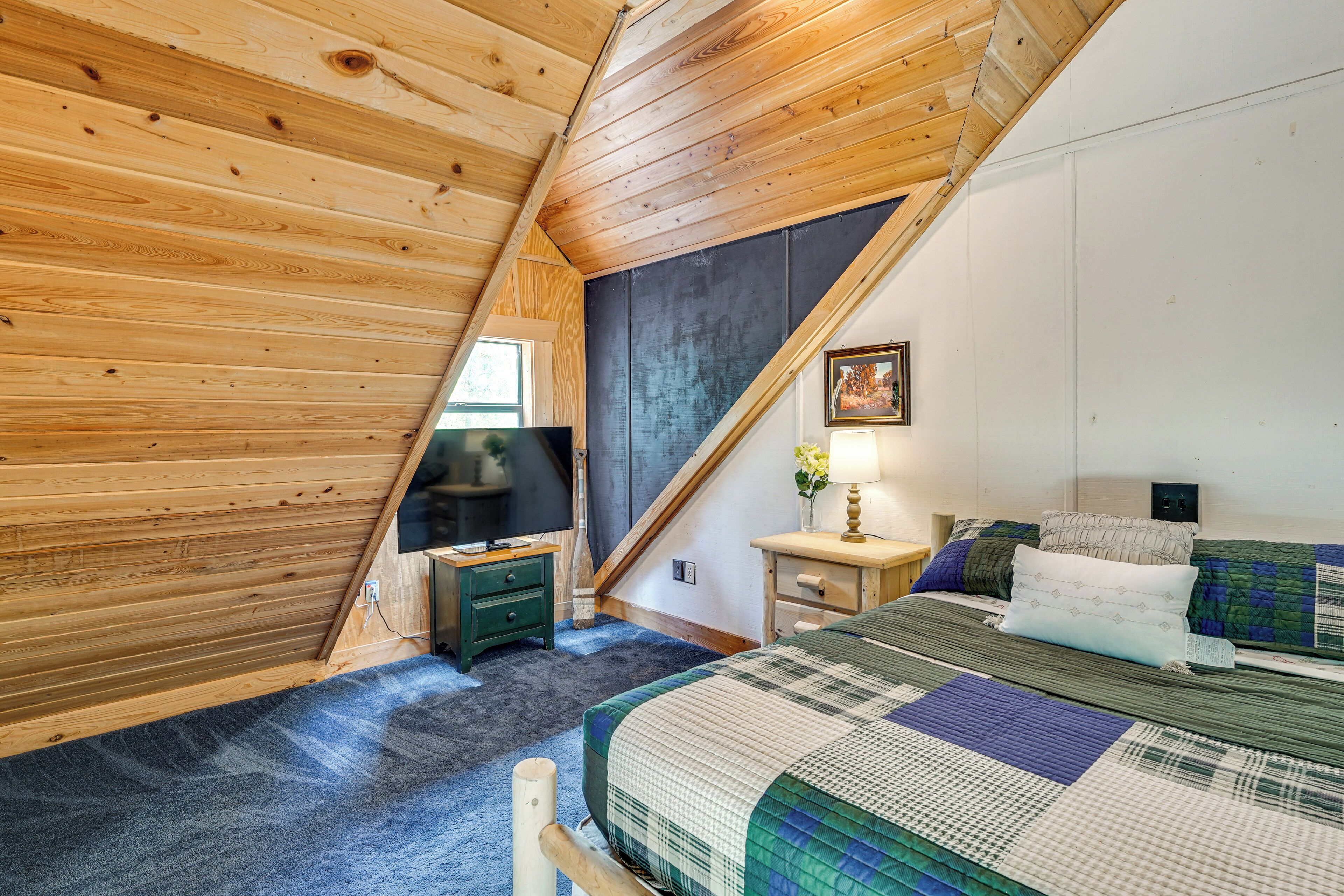A bedroom with a sloped ceiling, a bed with a quilt, a nightstand, a lamp, and a television.