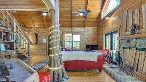 A log cabin interior with a stone fireplace, wooden floors, a red couch, and a ceiling fan. - Fish & Float at Natural Springs! Log Cabin in Bell (Bell)
