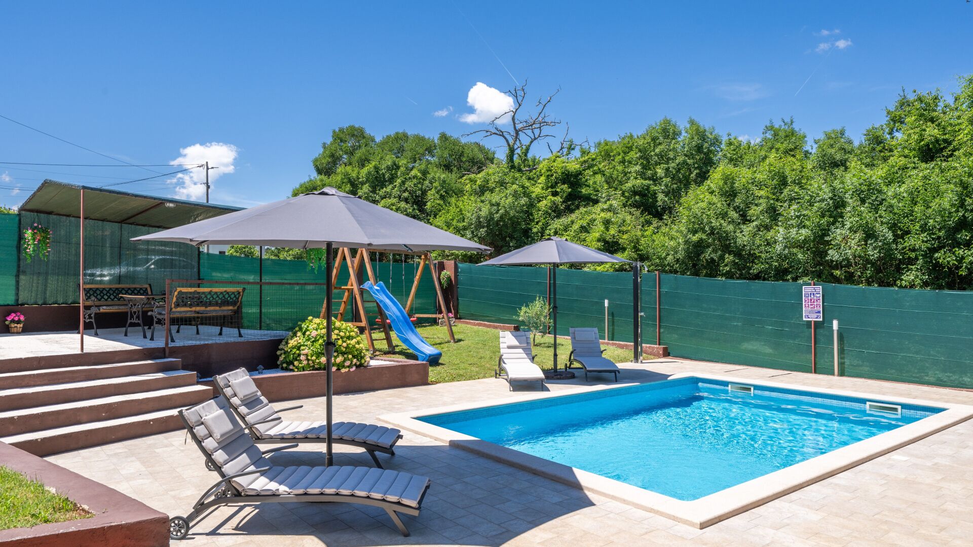 Un patio trasero con piscina, sillas de descanso, tobogán y un área de estar techada.