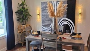 Een eethoek met een tafel voor vier personen, stoelen, een potplant en een decoratief wandobject.