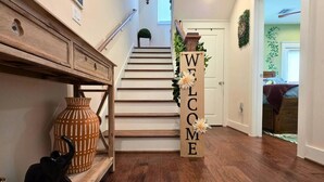 Een houten trap met een 'WELCOME' bord, een vaas en een beeldje van een zwarte kat.