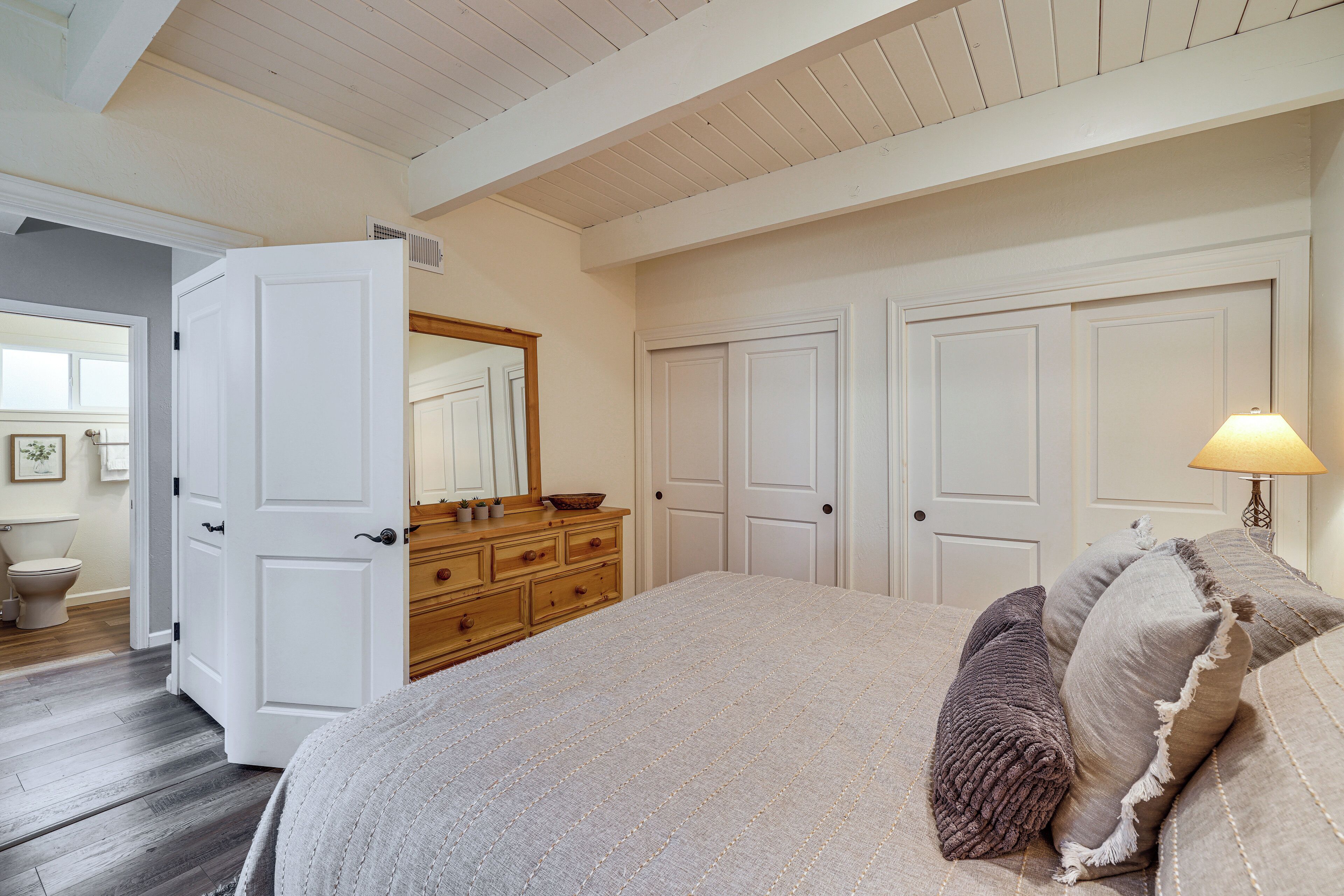 Un dormitorio con cama, cómoda, espejo y dos puertas.