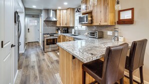 Eine Küche mit Holzschränken, Granit Arbeitsplatten, Edelstahlgeräten und einer Bar mit Ledersesseln.