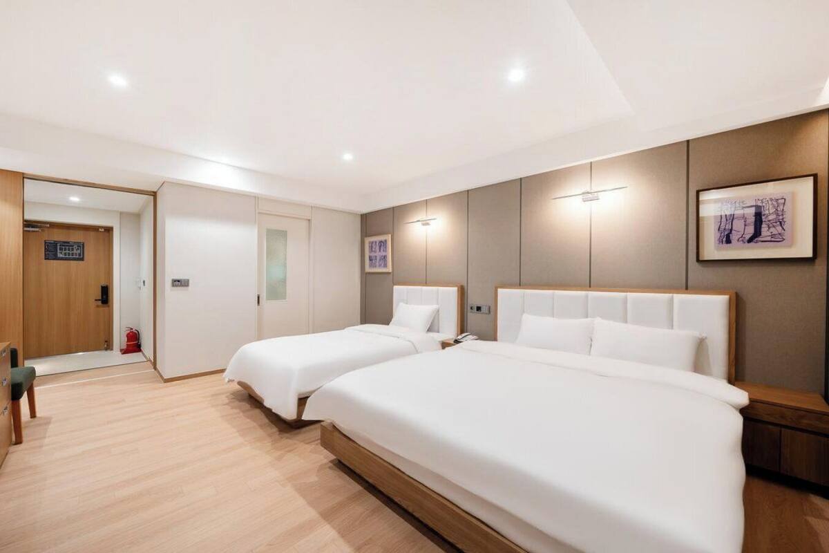 A hotel room with two beds, a desk, and a door leading to a hallway.