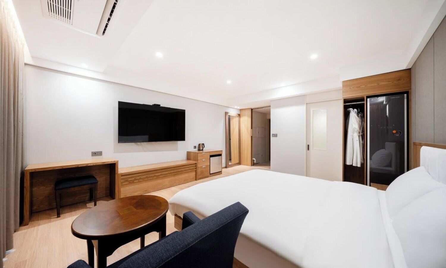 Una habitación de hotel moderna con una cama grande, televisión, escritorio y vestidor.