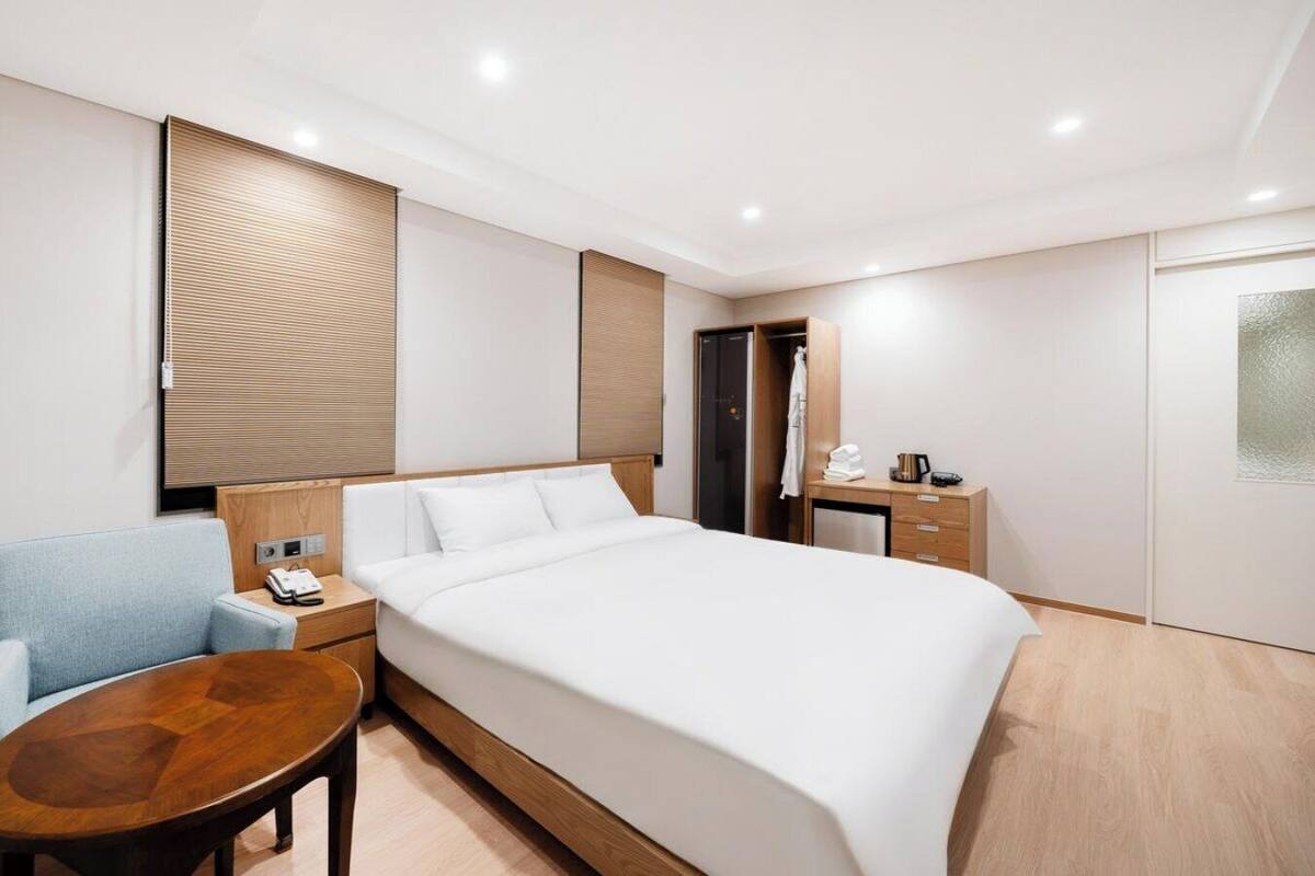 A hotel room with a bed, a desk, a chair, a bedside table, a wardrobe, and a bathroom door.
